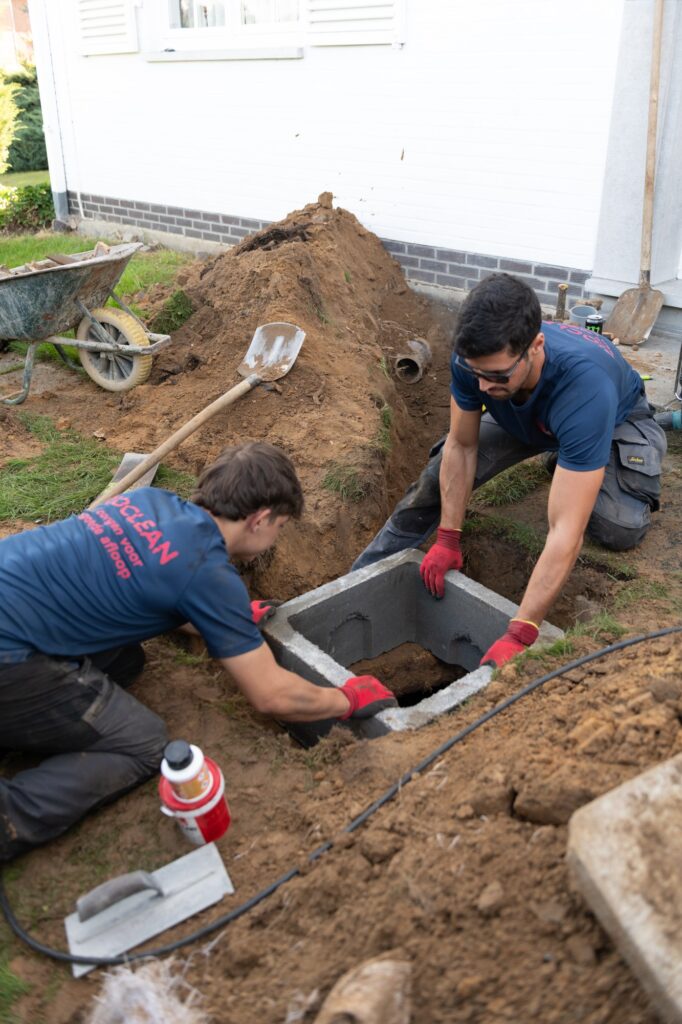 Twee Rioclean-medewerkers plaatsen een betonnen inspectieput in de uitgraving naast een woning