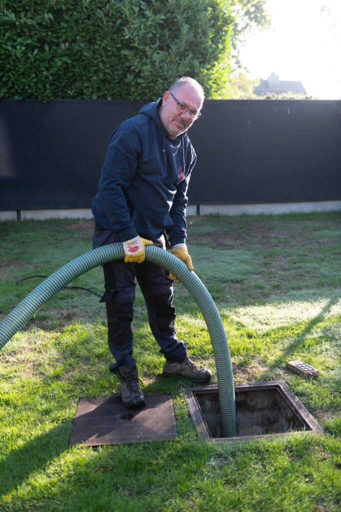 Rioclean-medewerker laat de zuigslang in een open septische put zakken
